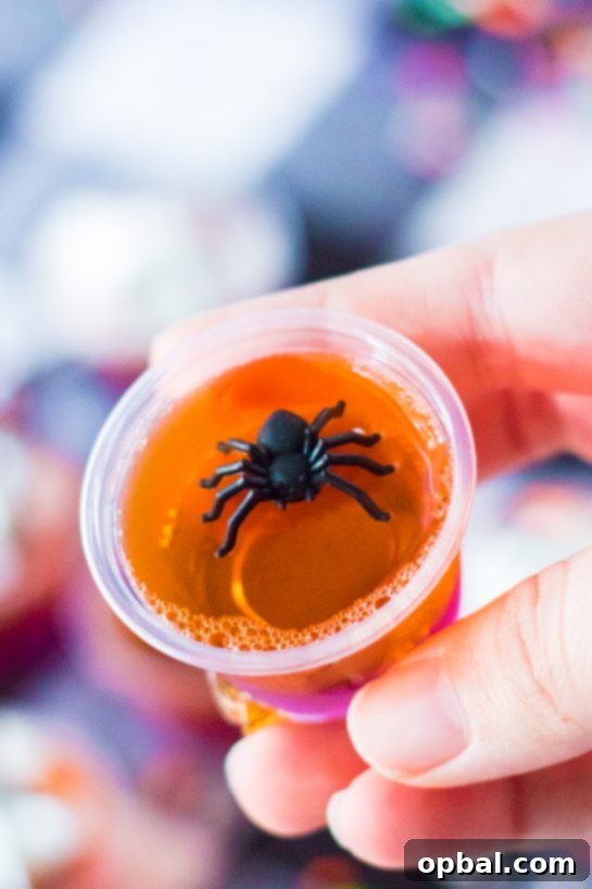 Halloween Spirit Shots 10 A captivating close-up of finished Halloween Jello Shots, adorned with playful plastic spiders, perfect for a themed party.