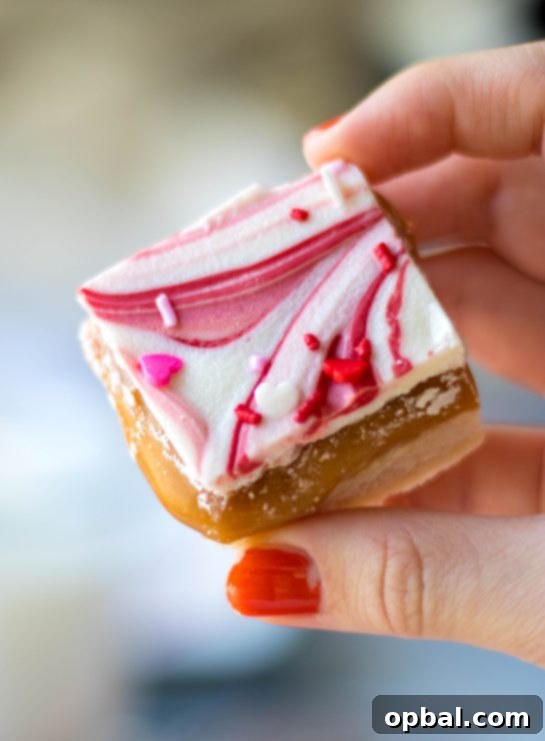 Sweet Valentine's Millionaire Bars 13 A mouth-watering close-up of a completed Valentine's Day Millionaire Bar, highlighting the vibrant swirls of pink and red chocolate and the generous topping of sprinkles.