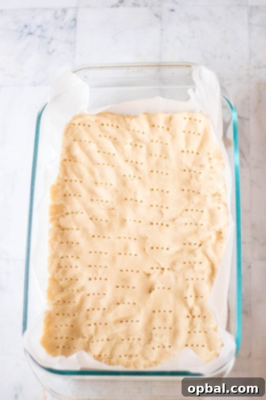 Sweet Valentine's Millionaire Bars 6 A close-up view of the baked shortbread base, uniformly pricked with a fork, preparing it for the layers of caramel and chocolate for the Valentine's Day Millionaire Bars.