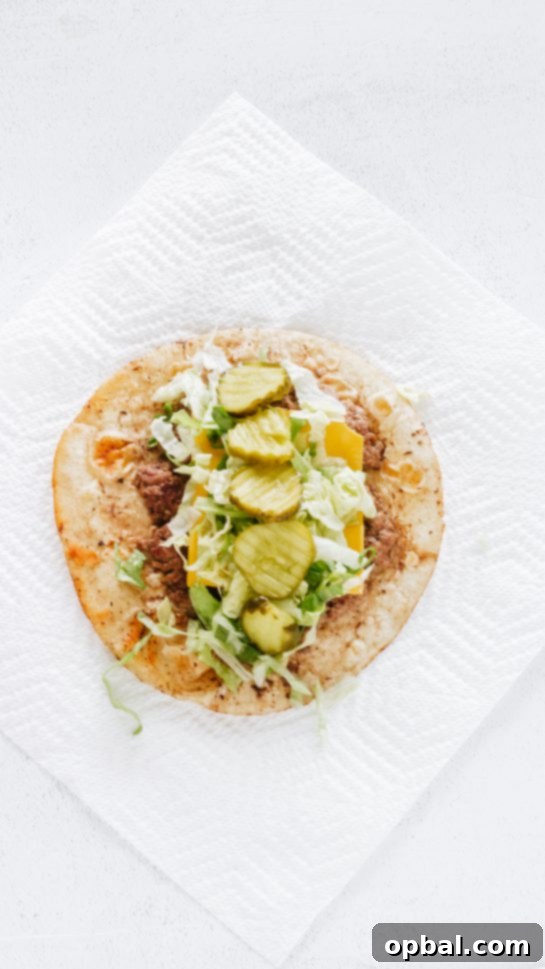 Viral Big Mac Tacos 6 Topping the cheesy ground beef with tangy dill pickle chips, an essential component for the authentic Big Mac flavor in these delicious tacos.