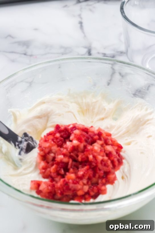 Strawberry Cloud Layer Cake 5 Chopped fresh strawberries being carefully mixed into the cake batter for the Strawberries & Cream Layered Cake recipe.