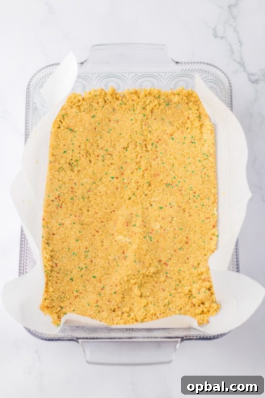 Yuletide Cookie Bliss 5 The process of pressing the crushed cookie crust firmly into the baking pan, creating the solid foundation for the layered Christmas Cookie Lush.