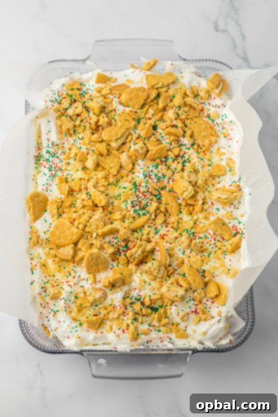 Yuletide Cookie Bliss 8 Sprinkling a generous amount of crushed Oreo cookies over the whipped topping layer of the Christmas Cookie Lush, adding a final touch of texture and flavor.