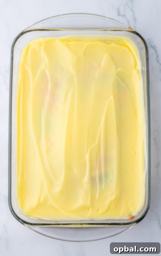 Springtime Easter Poke Cake 7 Spreading the white chocolate layer on colored batter for the Easter poke cake recipe after it comes out of the oven.