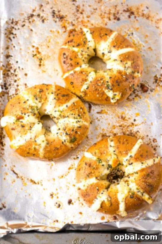TikTok Stuffed Bagels, sliced and ready to be filled with sweetened cream cheese, then brushed with garlic butter and sprinkled with parmesan cheese before baking.
