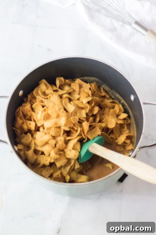 Mixing Fritos with the creamy peanut butter base, a crucial step in preparing the Frito Candy recipe for Christmas, ensuring each chip is coated.