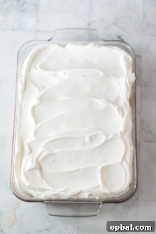 Holiday Spirit Poke Cake 7 Photo of frosting the Christmas Poke Cake with the whipped cream frosting